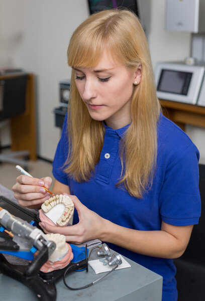 Dental lab technician applying porcelain to dentition mold