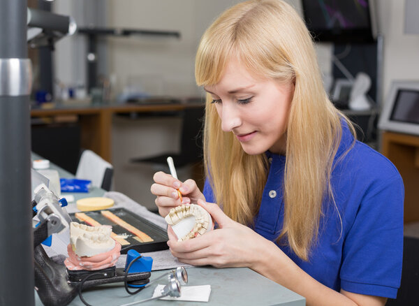 Dental lab technician applying porcelain to dentition mold