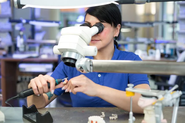 Técnico dentário produzindo uma prótese sob um microscópio — Fotografia de Stock