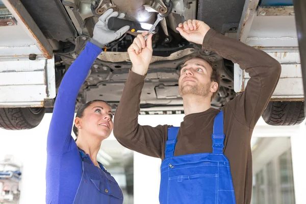 Two mechanics repairing a car in hydraulic lift — Stock Photo, Image