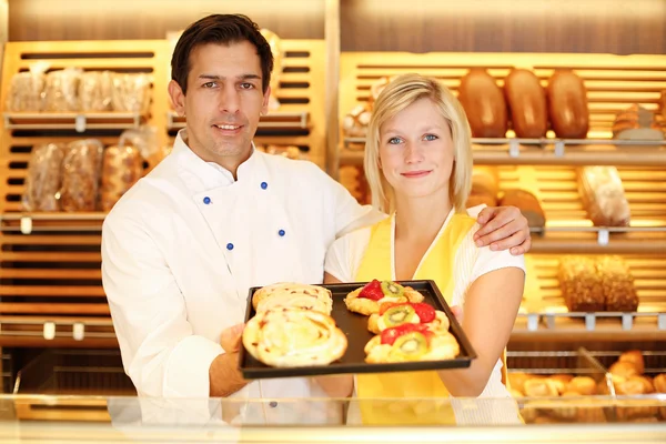 Baker and shopkeeper in bakery with tablet of cake — Stock Photo, Image