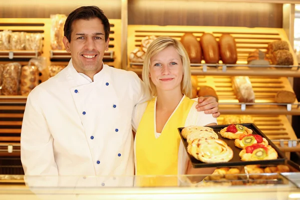 Baker and shopkeeper in bakery with tablet of cake — Stock Photo, Image