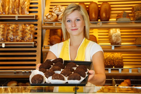 Shopkeeper in bakery presents tablet of rum balls — Stock Photo, Image