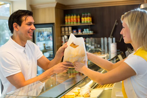 Shopkeeper giving pastry to customer — Stock Photo, Image