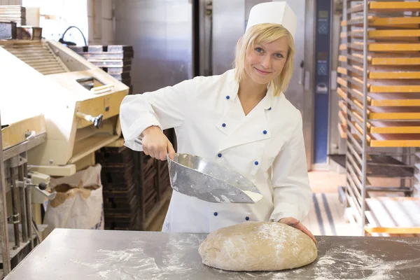 Baker pouring flour on bread dough in bakery — Stock Photo, Image