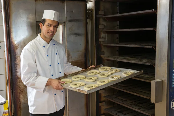 Baker putting pretzels into oven in a bakery — Stock Photo, Image