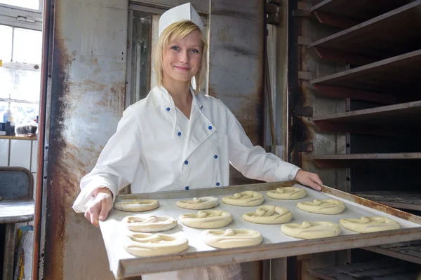 Baker putting pretzels into oven in a bakery — Stock Photo, Image