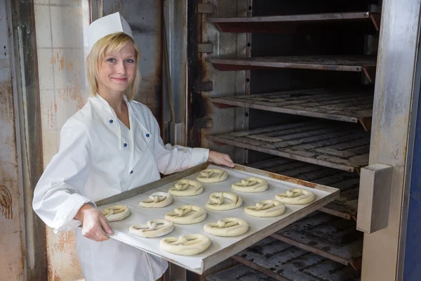 Baker putting pretzels into oven in a bakery — Stock Photo, Image