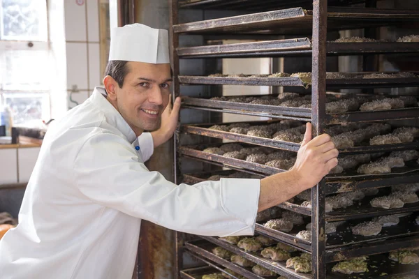 Baker putting a rack of bread into oven — Stock Photo, Image