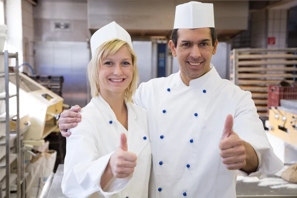 Two bakers showing thumbs up in bakeshop — Stock Photo, Image
