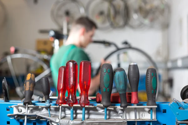 Werkzeug in einer Werkstatt, im Hintergrund repariert ein Fahrradmechaniker ein Rad — Stockfoto