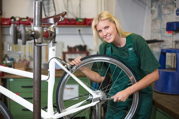 Vrouwelijke monteur in werkplaats die een fietswiel repareert — Stockfoto