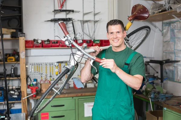 Bicycle mechanic carrying a bike in workshop — Stock Photo, Image