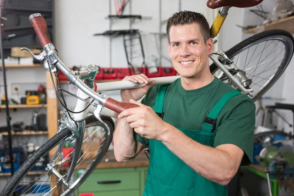 Cykel mekaniker bär en cykel i workshop leende — Stockfoto