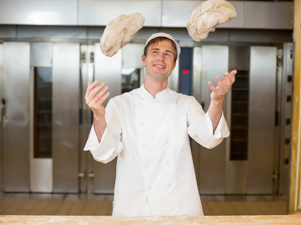 Baker throwing dough into air in bakehouse — Stock Photo, Image