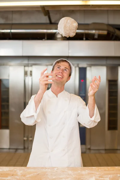 Baker deeg gooien in de lucht in bakkerij — Stockfoto