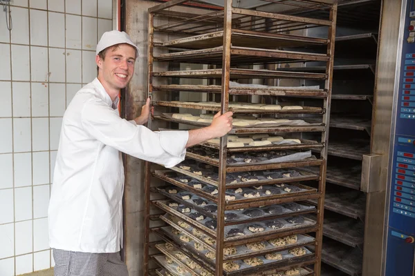 Baker pushing rack full of bread into the oven — Stock Photo, Image