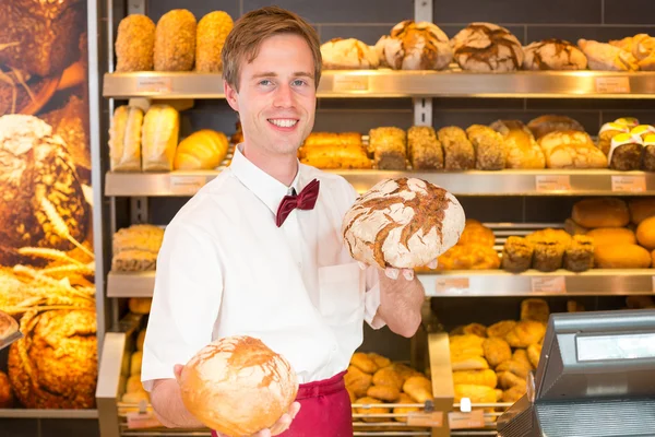 Salesman in bakery holding different types of bread — Stock Photo, Image