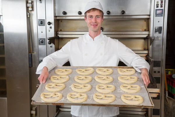 Padeiro na padaria com assadeira cheia de pretzels — Fotografia de Stock
