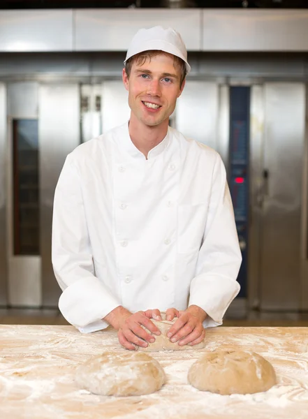 Lächelnder Bäcker knetet Teig in Bäckerei Stockfoto