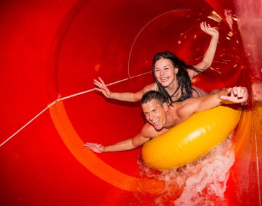 Couple in water slide at public swimming pool clipart
