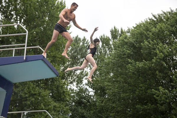 Casal pulando de uma prancha de mergulho em uma piscina — Fotografia de Stock