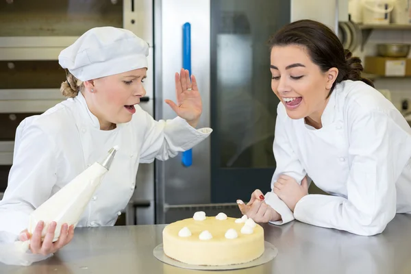 Confectioner apprentice nibbling whipped cream from cake — Stock Photo, Image