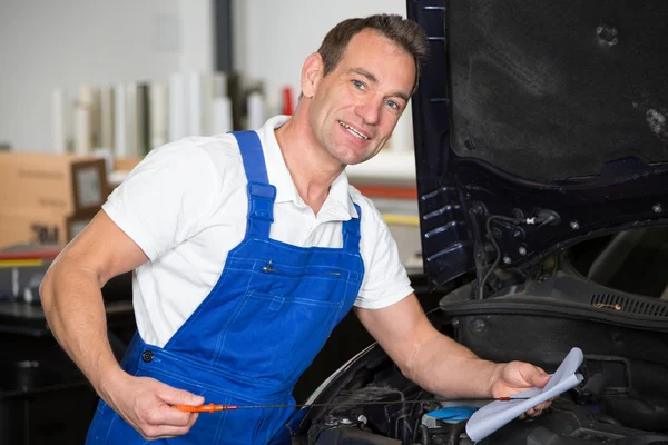 Mechanic checking oil levels at a car in garage — Stock Photo, Image