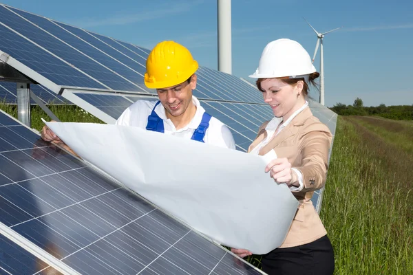 Photovoltaic engineers with construction plan at solar panels — Stock Photo, Image