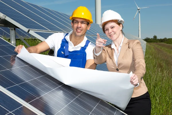 Photovoltaic engineers with construction plan at solar panels — Stock Photo, Image