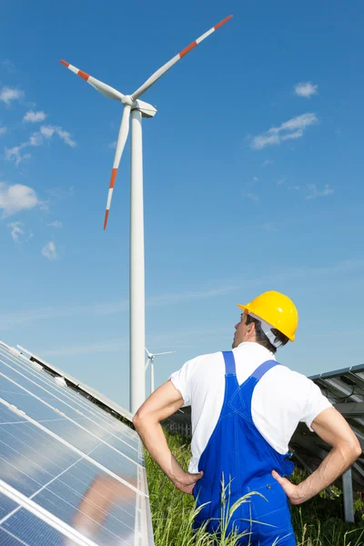 Engineer in front of solar panels looks at wind turbine — Stock Photo, Image