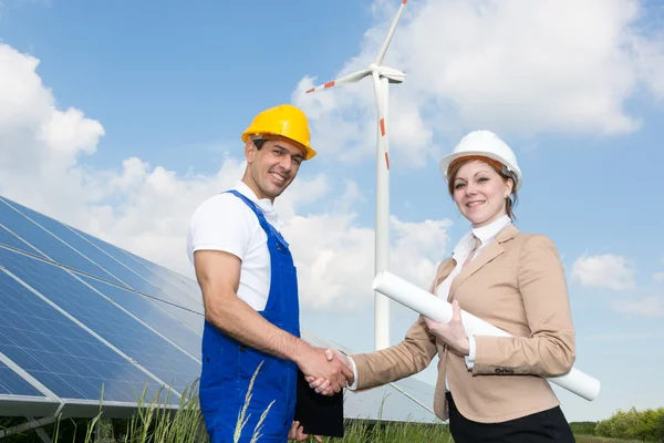 Des ingénieurs serrent la main devant des panneaux solaires et des éoliennes — Photo