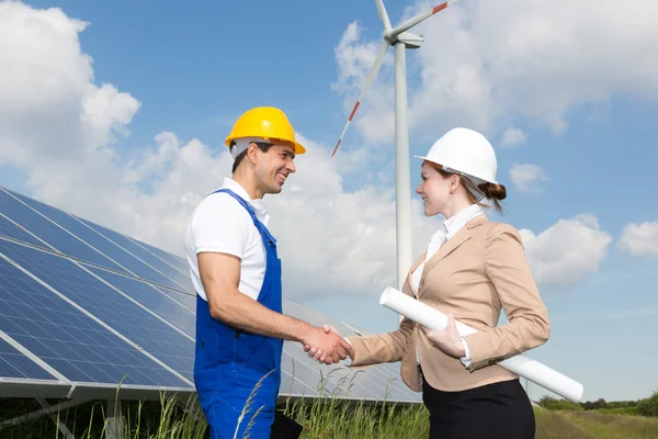 Engineers shake hands in front of solar panels and wind turbine — Stock Photo, Image