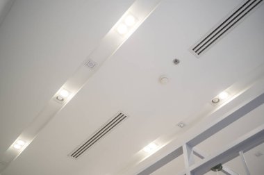 Tavana monte edilmiş kaset tipi klima ve beyaz tavanda modern lamba ışığı. Ev ya da ofis için havalandırma kanalı
