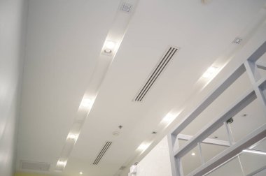 Tavana monte edilmiş kaset tipi klima ve beyaz tavanda modern lamba ışığı. Ev ya da ofis için havalandırma kanalı