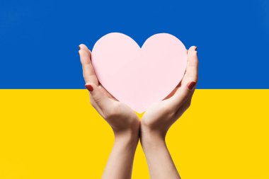 Ukrayna bayrağının arka planında kalp şeklinde kağıt tutan kadınlar. Ukrayna sembolü ile kal. El kalp aşk jesti Ukrayna bayraklı.