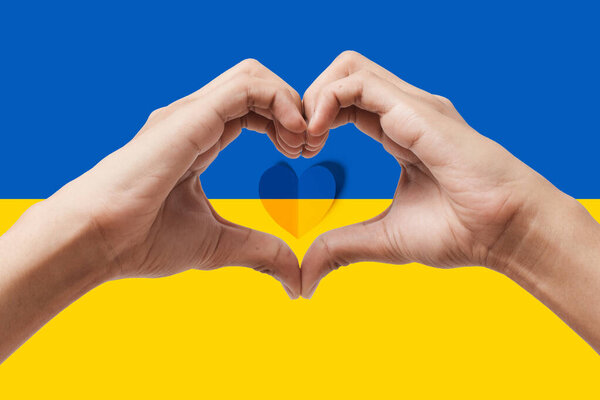 Мужские руки делают сердечную форму на фоне флага Украины. Оставайся с украинским символом. Ручной жест любви на фоне украинского флага.