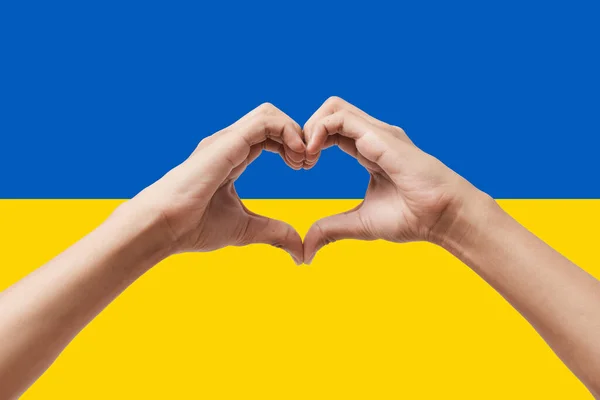 Man hands making a heart shape on Ukraine flag color background. Stay with ukraine symbol. Hand heart love gesture with ukrainian flag background.