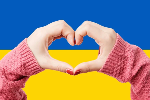 Women hands making a heart shape on Ukraine flag color background. Stay with ukraine symbol. Hand heart love gesture with ukrainian flag background.