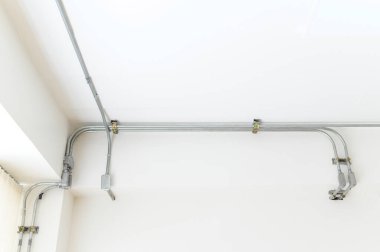 Electrical wires and pipes on house concrete ceiling background, plastic hoses with cables in empty room. Lines of pvc tubes, conduit after professional work. Renovation of home or factory interior.