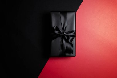 Kırmızı ve siyah arkaplanda siyah kurdeleli siyah hediye kutusunun üst görüntüsü. Alışveriş konsepti boks günü ve Kara Cuma indirimli kompozisyon.