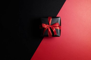 Kırmızı ve siyah arka planda izole edilmiş kırmızı kurdeleli siyah hediye kutusunun üst görüntüsü. Alışveriş konsepti boks günü ve Kara Cuma indirimli kompozisyon.