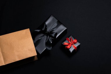 Kırmızı, alışveriş çantası ve siyah arka planda izole edilmiş siyah kurdeleli hediye kutusunun üst görüntüsü. Alışveriş konsepti boks günü ve Kara Cuma indirimli kompozisyon.