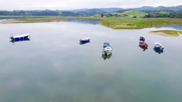 Los barcos de pesca están en una tranquila bahía tranquila. Agua del espejo. Pequeño pueblo de pescadores junto al océano. Nublado día de mal humor en la costa. Hermoso paisaje costero con verdes prados y montañas. Cantabria. — Vídeos de Stock