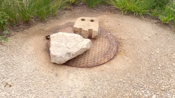 Le vieux trou d'homme tremble de la pression de l'intérieur. La trappe métallique est pressée contre les pierres. Travaux routiers. — Video