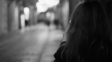 Long-haired woman in a long black coat walks around the city and takes a photo with a smartphone. A pleasant walk through the beautiful old town. Black and white footage.