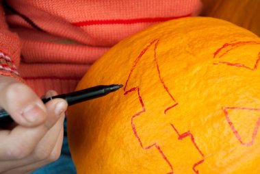 Kız masaya oturur ve bir kalemle bir balkabağını kesmek için bir çizgi çizer. Cadılar Bayramı 'nı kutlayalım. Bir kriko feneri yap..