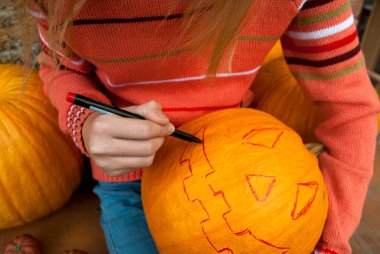 Kız masaya oturur ve bir kalemle bir balkabağını kesmek için bir çizgi çizer. Cadılar Bayramı 'nı kutlayalım. Bir kriko feneri yap..