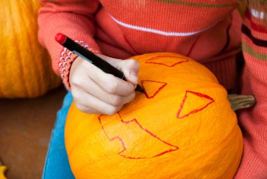 Kız masaya oturur ve bir kalemle bir balkabağını kesmek için bir çizgi çizer. Cadılar Bayramı 'nı kutlayalım. Bir kriko feneri yap..