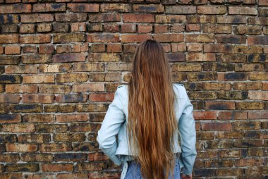 Kadın sırtı kameraya dönük duruyor. Güzel, uzun saçlar. Tuğla bir duvarın arka planında sarışın. 